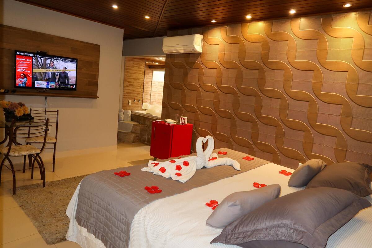 Une chambre d’hôtel avec un grand lit, un téléviseur fixé au mur, une valise rouge et un mur orné d’un motif géométrique.