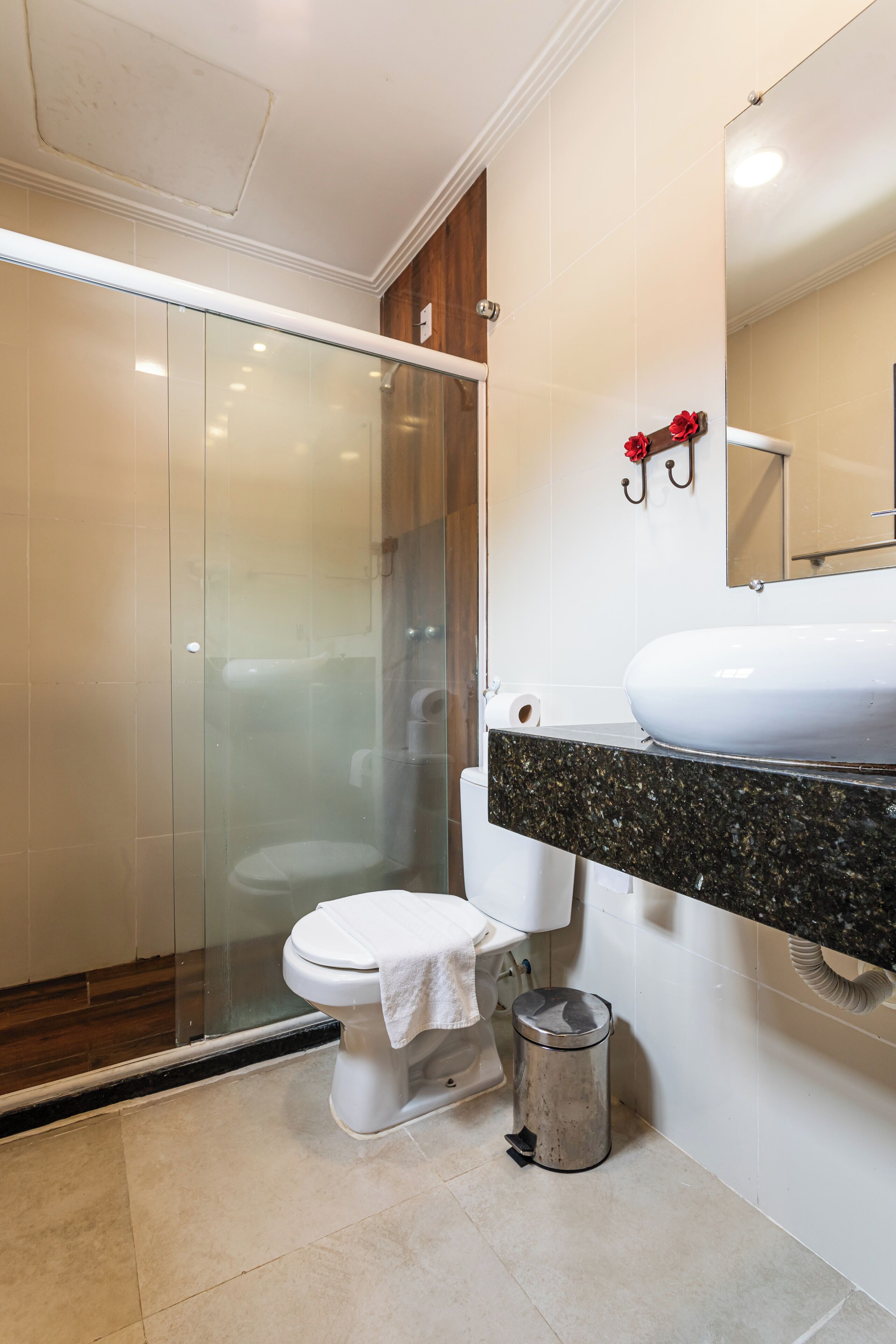 Un baño moderno con mampara de vidrio, inodoro blanco, lavamanos con encimera de granito y un cubo de basura.