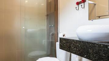 Un baño moderno con mampara de vidrio, inodoro blanco, lavamanos con encimera de granito y un cubo de basura.