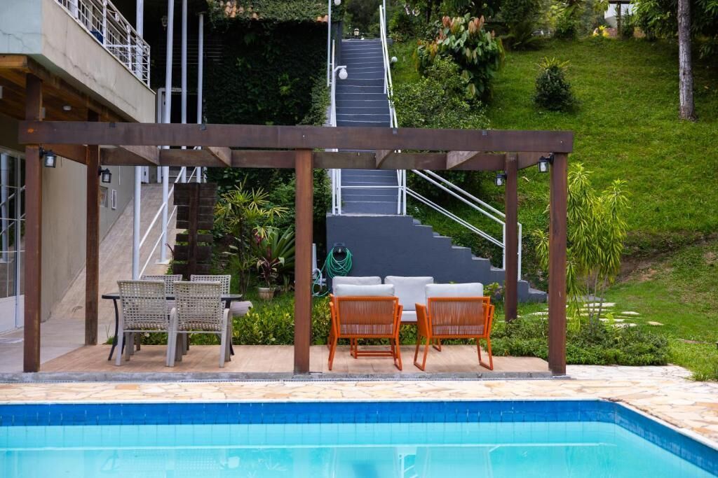 A pool area with a pergola, two wicker chairs, a table, and a staircase leading to a higher level.