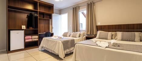 A hotel room with two beds, a wardrobe, a small fridge, and a ceiling fan.