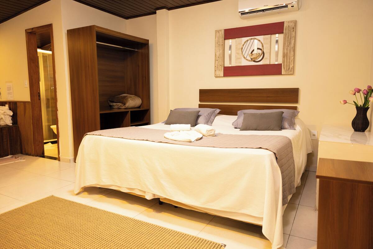 Un lit bien fait, recouvert d’une couvre-lit blanche et beige, avec une tête de lit en bois et une horloge fixée au mur.