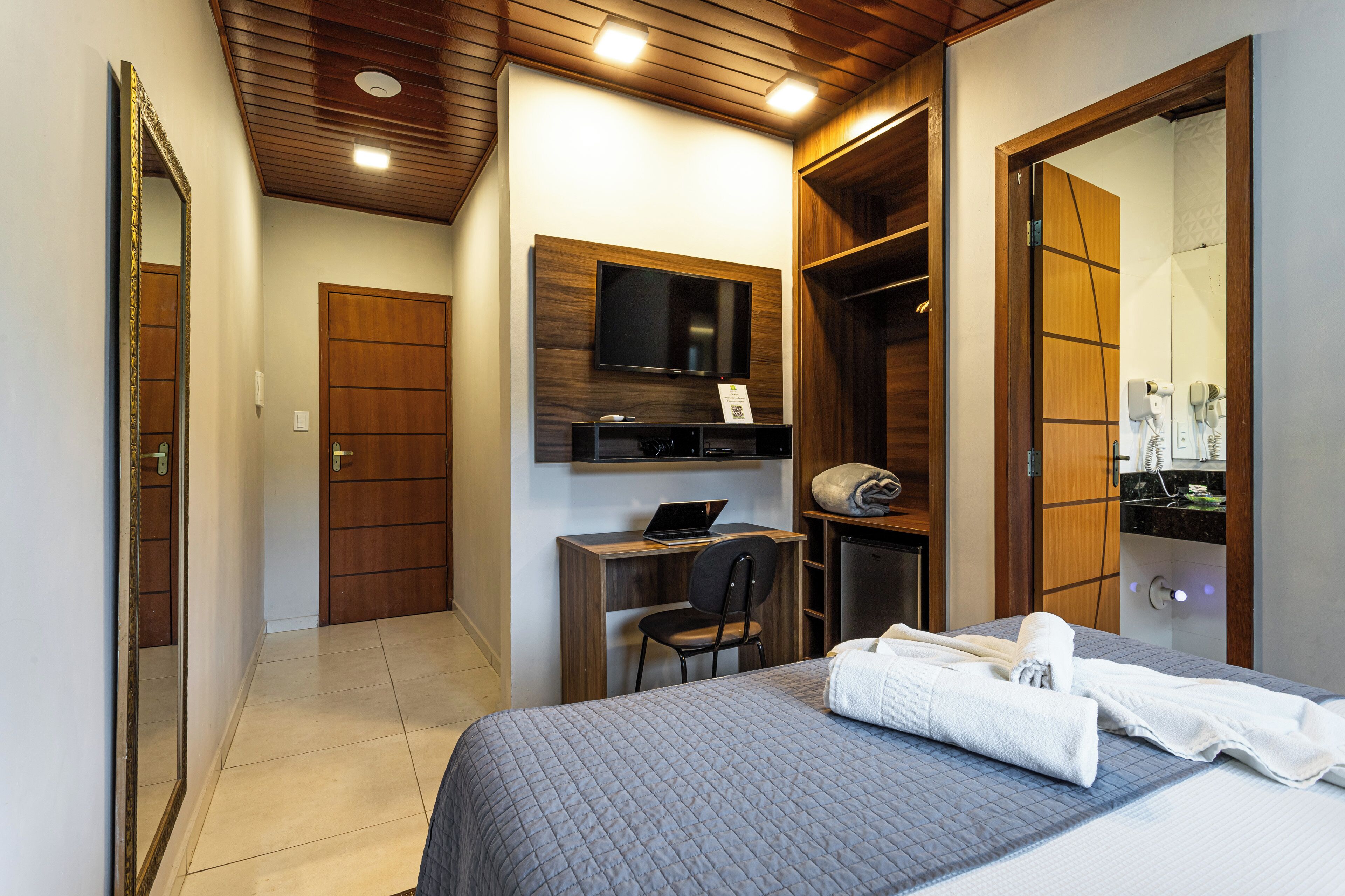 Un dormitorio con cama, escritorio con computadora portátil, silla, televisor y armario.
