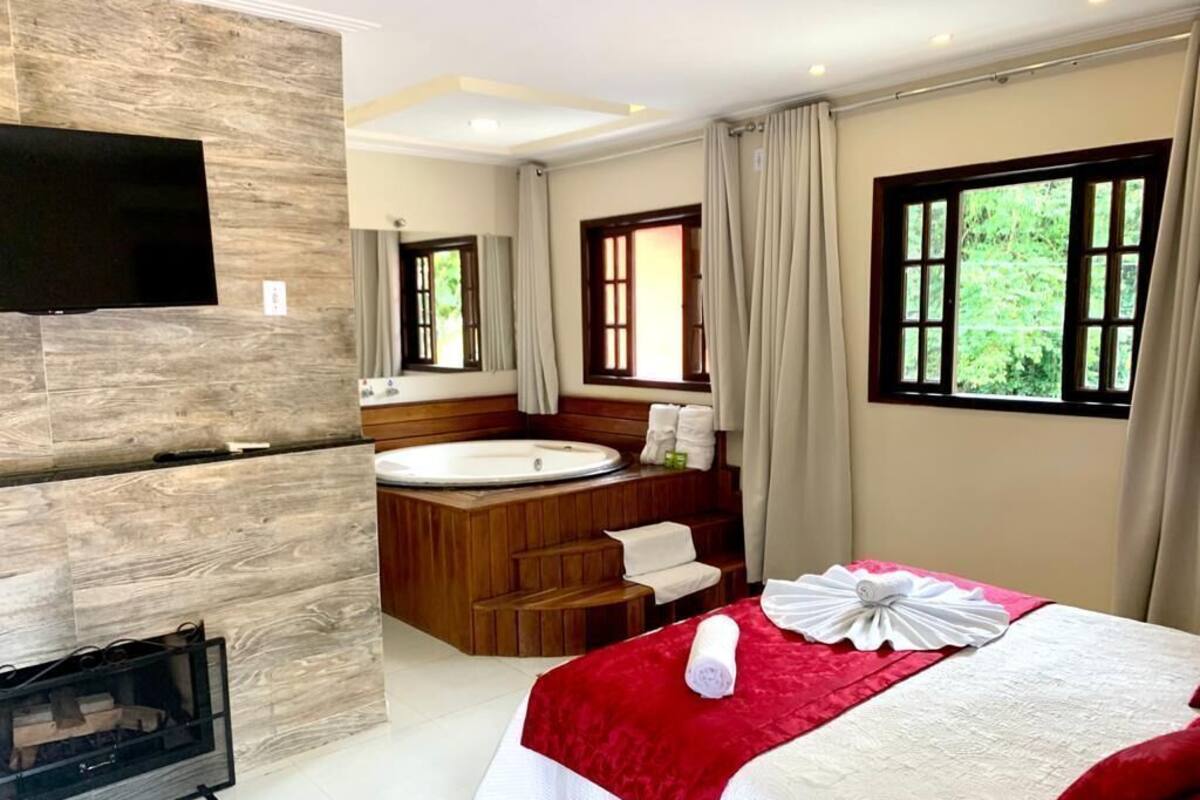 Une chambre d’hôtel avec un grand lit, un espace de baignade avec des éléments en bois, une télévision et une fenêtre avec des rideaux.