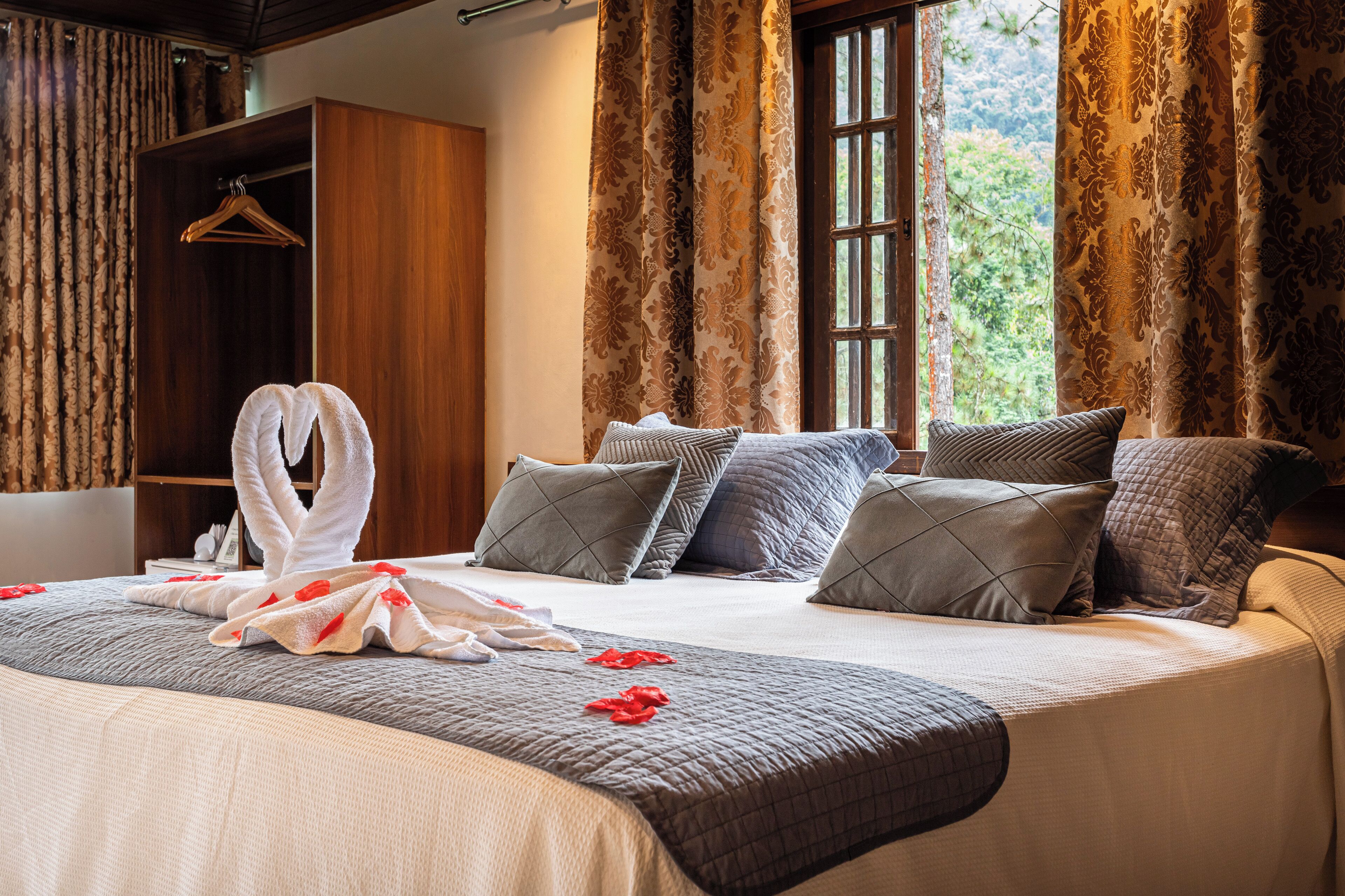 Una cama bien hecha con un arreglo de toallas, un armario de madera y una ventana con cortinas.