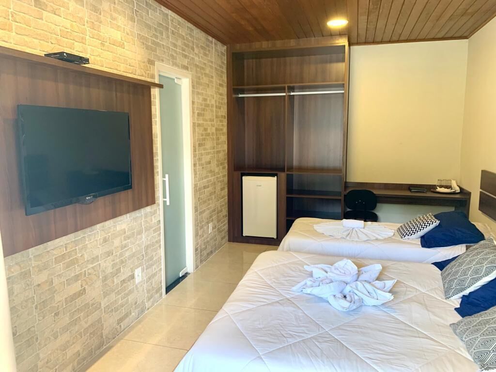 A hotel room with two beds, a TV mounted on the wall, a wardrobe, and a desk with a chair.