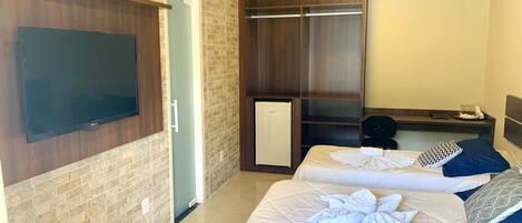 A hotel room with two beds, a TV mounted on the wall, a wardrobe, and a desk with a chair.