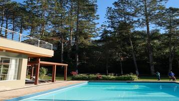 Una piscina con bordo in legno e area coperta, circondata da alberi alti.