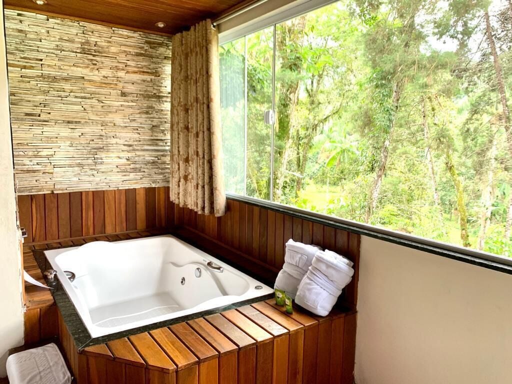 Eine Holzhütte mit einer großzügigen Badewanne, einer Steinsäule und einem Fenster mit Blick auf einen Wald.