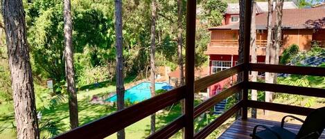 A wooden deck with chairs overlooking a swimming pool and lush greenery.