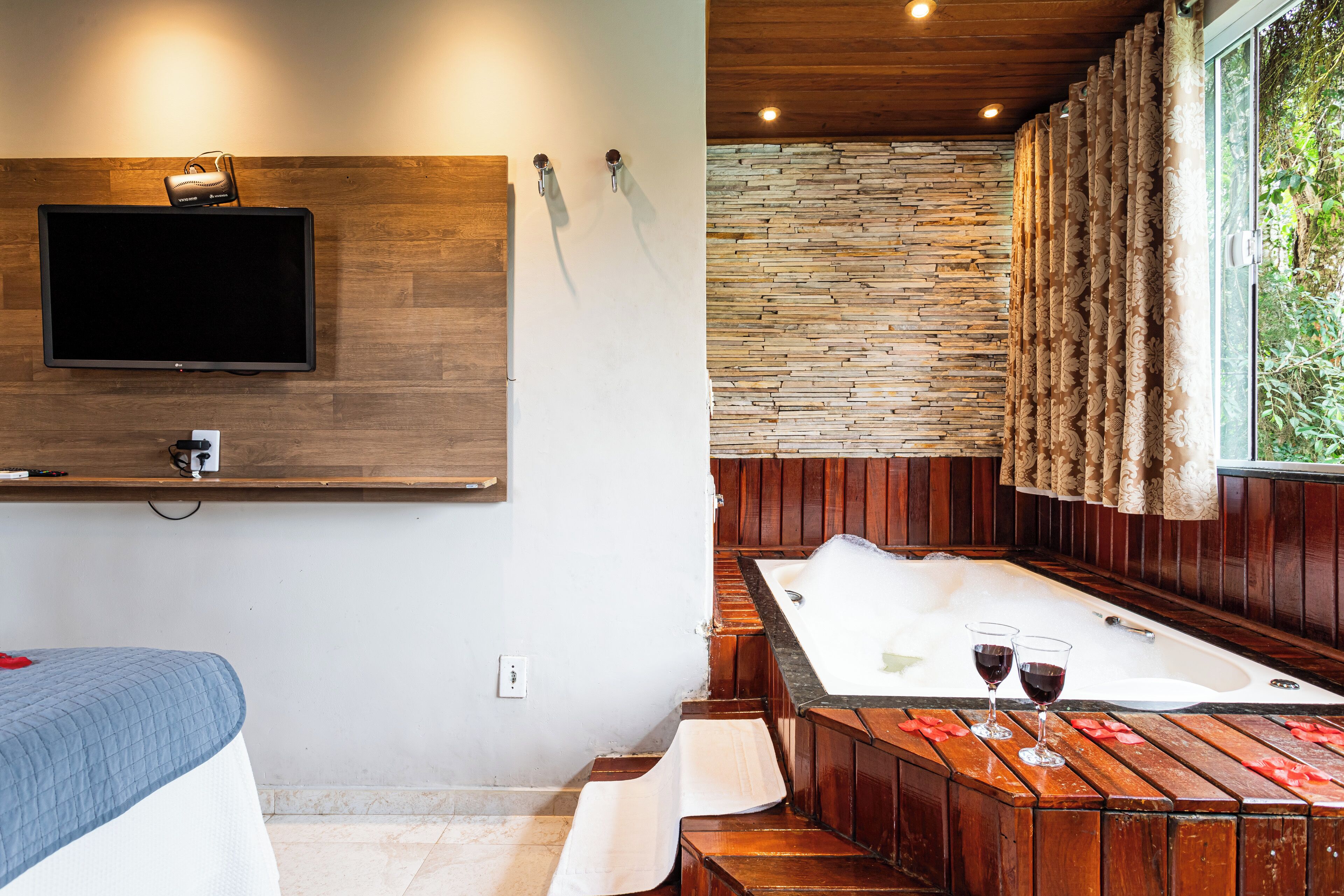Une salle de bain moderne avec un meuble-lavabo en bois, une grande baignoire et un téléviseur fixé au mur.