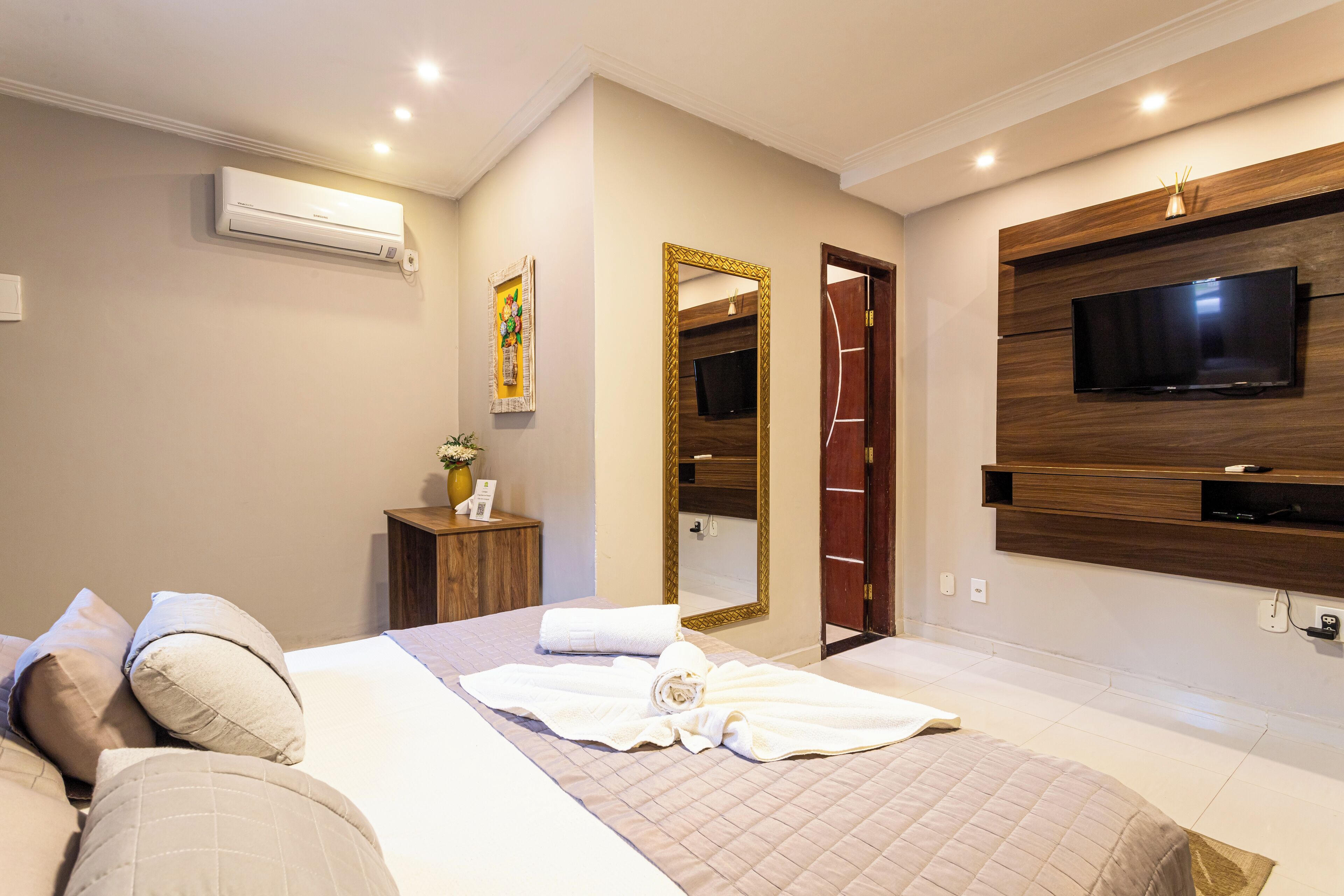 Una habitación de hotel moderna con cama, televisor, espejo y aire acondicionado.