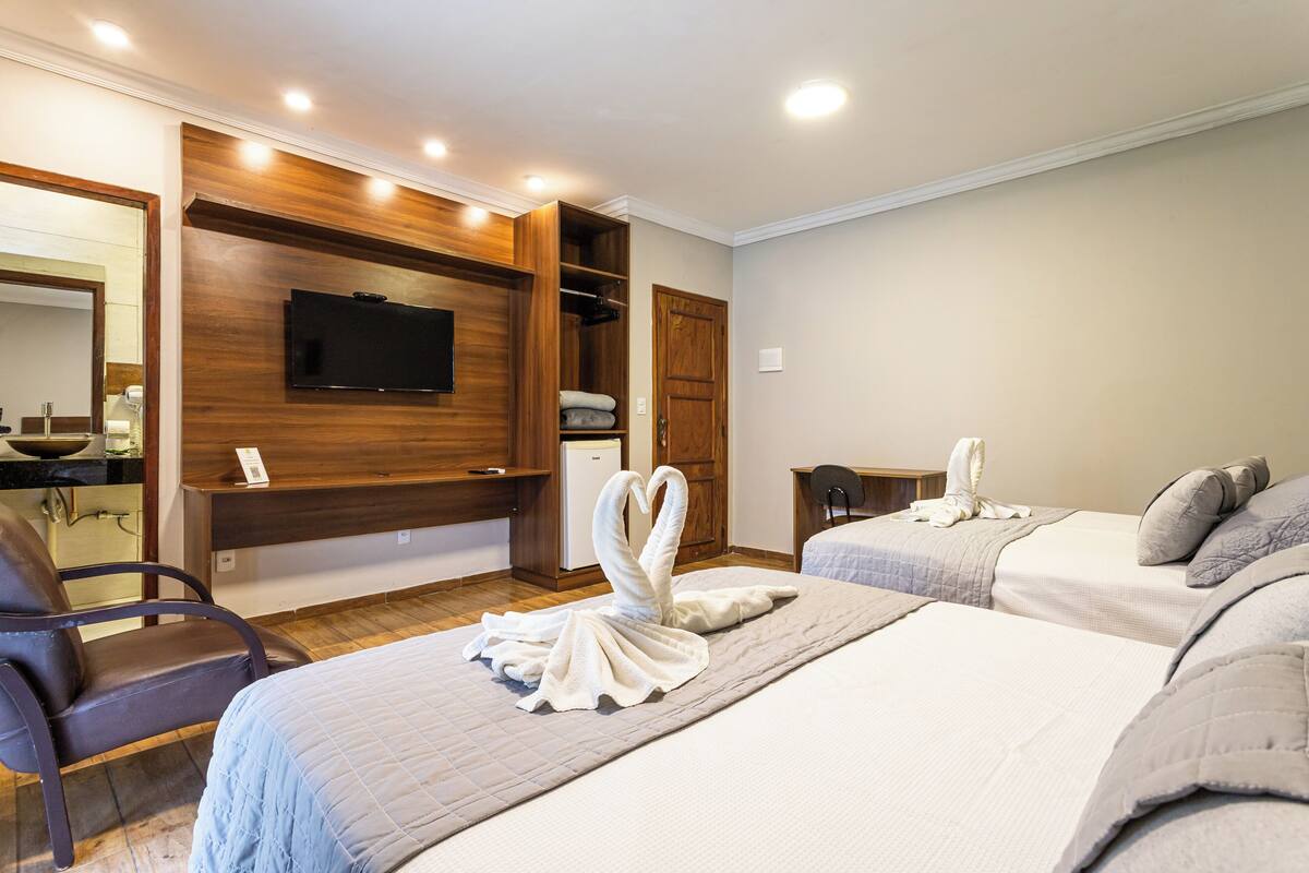Une chambre d’hôtel équipée d’un téléviseur fixé au mur, d’une armoire en bois, d’un lit avec des serviettes, d’une chaise et d’un bureau.