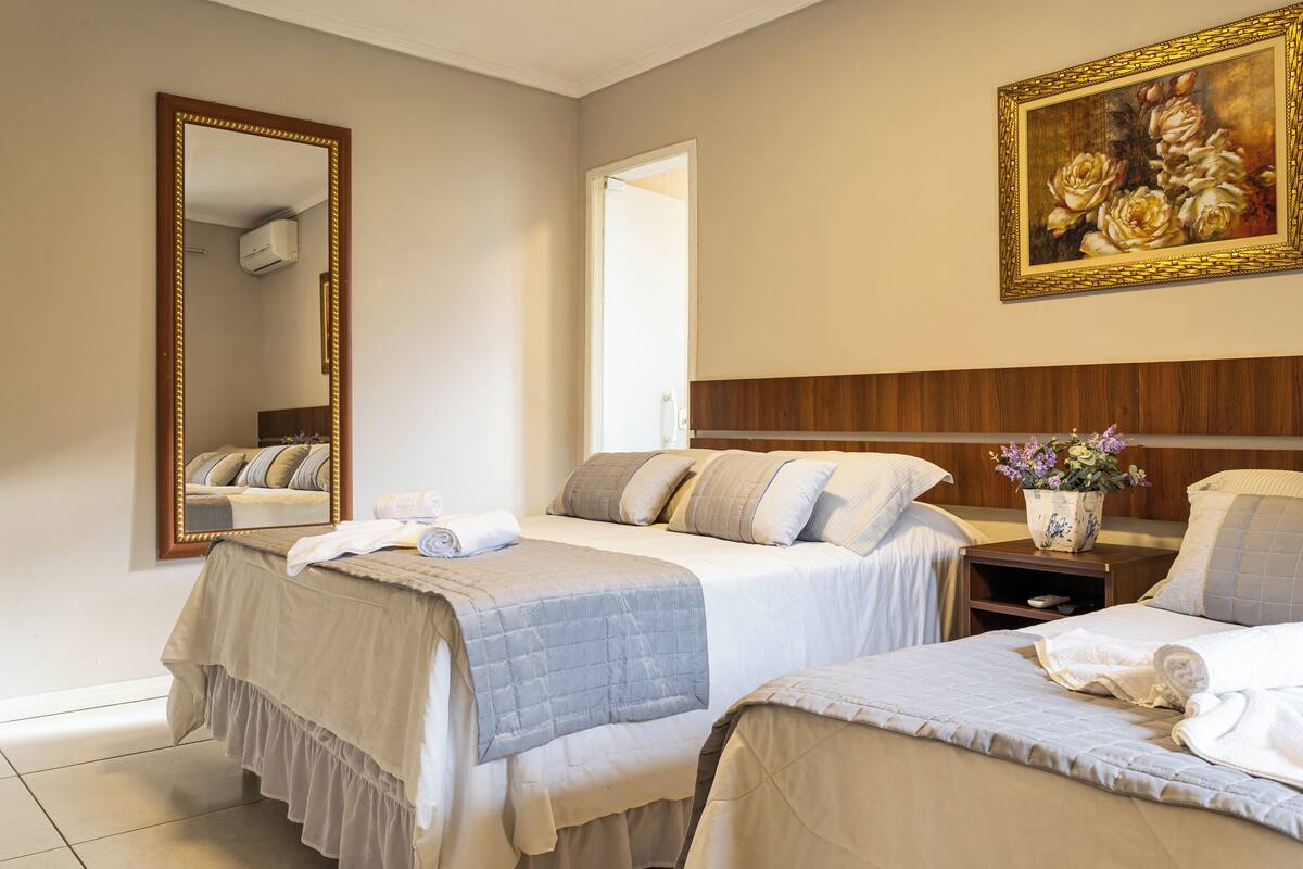 Une chambre d’hôtel avec deux lits, un grand miroir, un tableau et une table de chevet ornée d’un vase de fleurs.