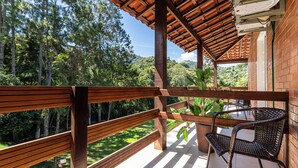 A wooden balcony with a view of a lush forest, a table with chairs, and a brick wall. - Pousada Recanto de Moriá (Itatiaia)