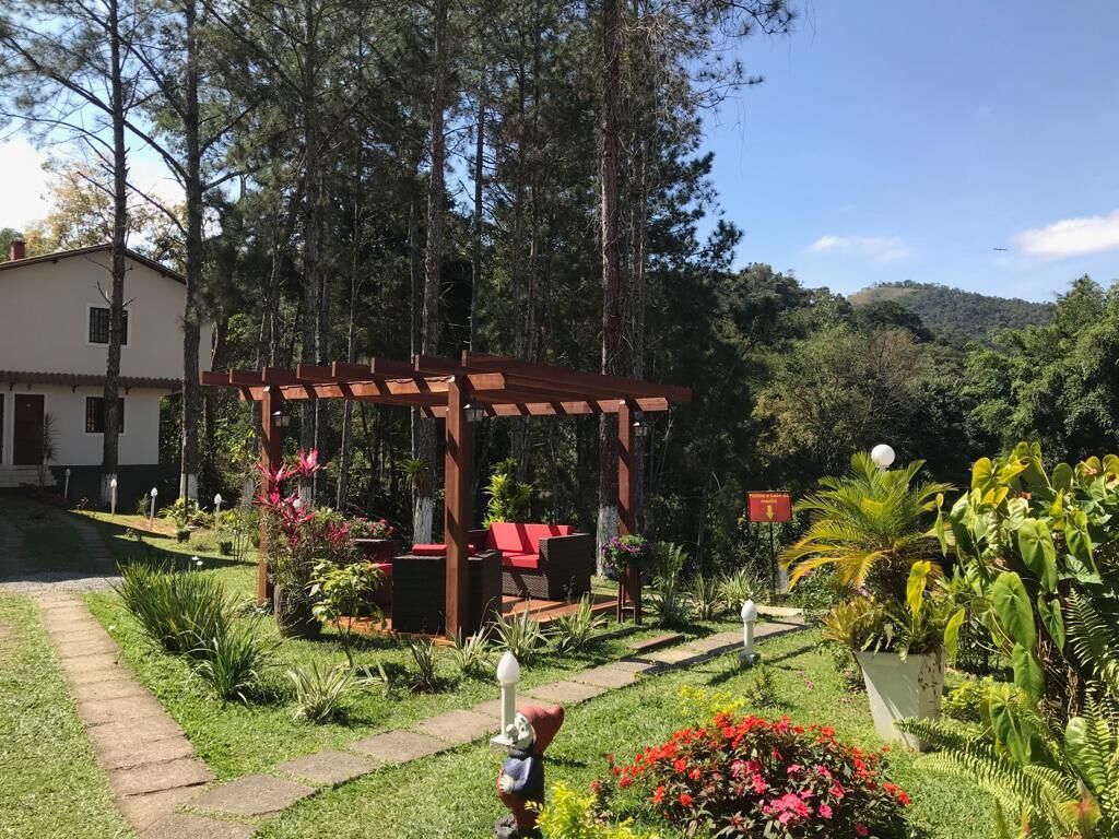 Un jardín con un pérgola de madera, asientos exteriores y diversas plantas.