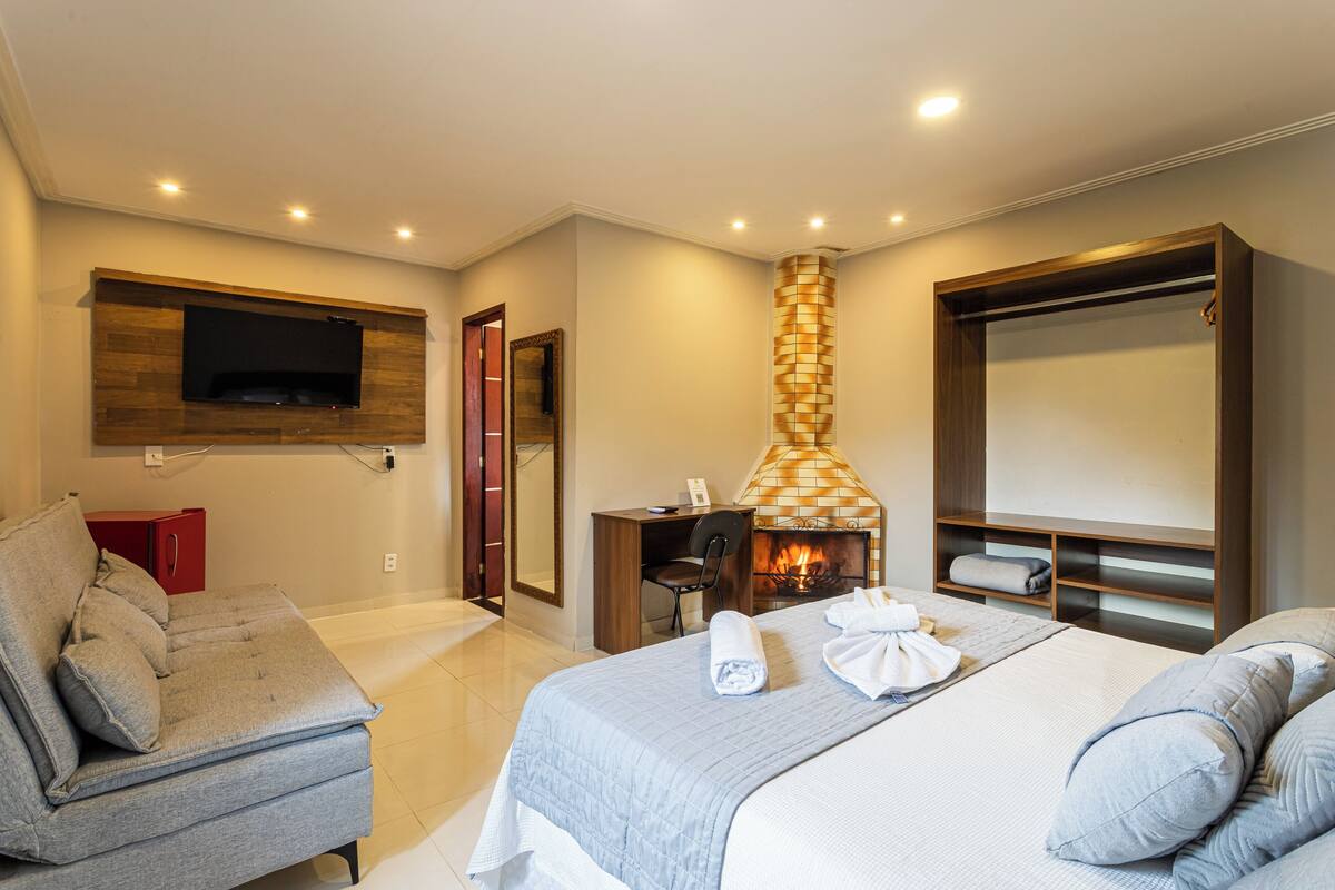 Une chambre d’hôtel moderne équipée d’un lit, d’un canapé, d’un téléviseur fixé au mur, d’une cheminée et d’un bureau avec une chaise.