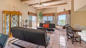 A spacious living area with a black sofa, a dining table with chairs, a wooden cabinet with glass doors, and a ceiling fan. - Tucson Hilltop Estate: Sleeps 9, Heated Pool  & Spa, Game Room, Cantina, Gas BBQ (Tucson)