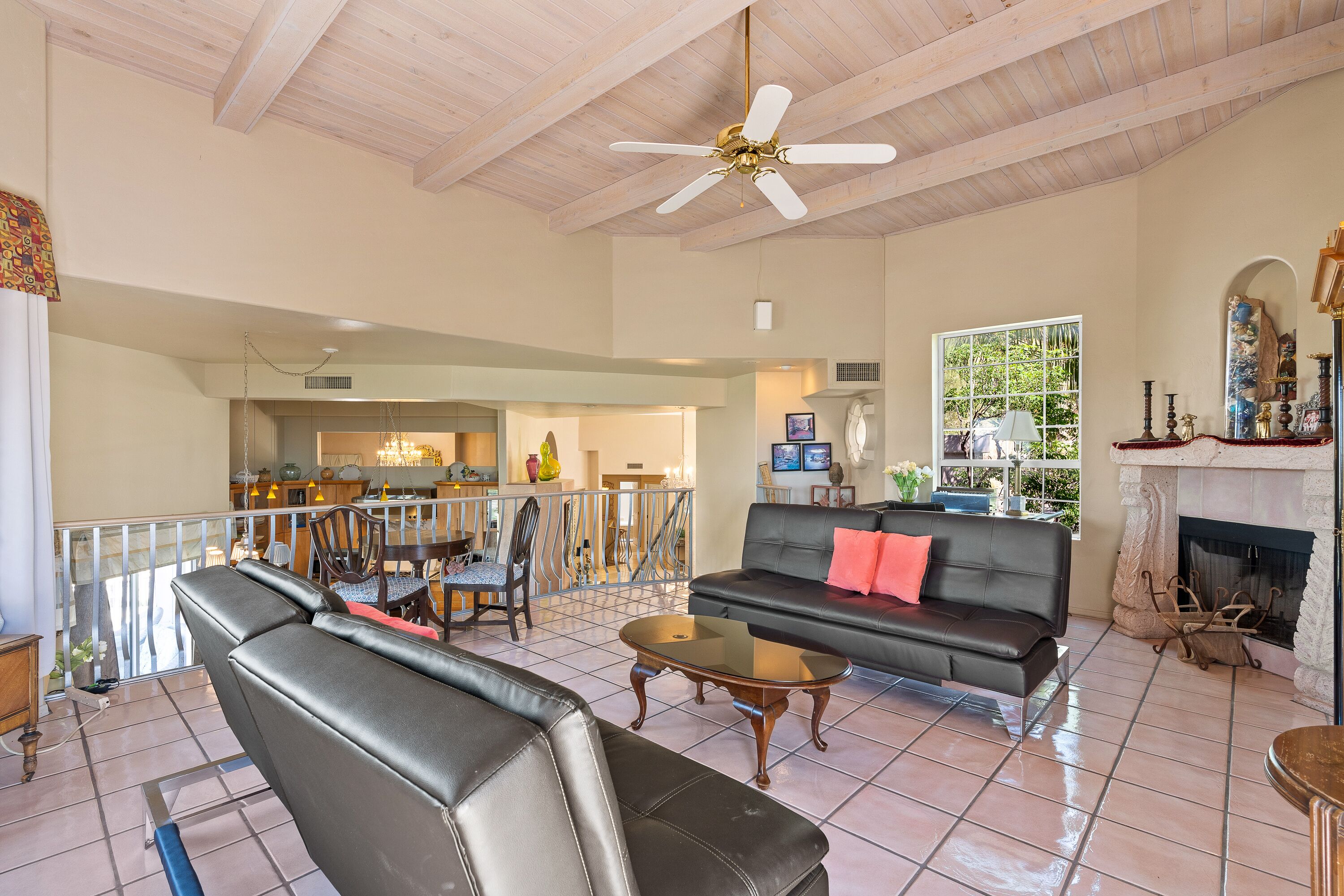 A spacious living room with a black leather sofa, a glass coffee table, and a ceiling fan.