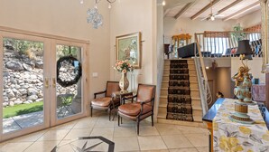 A spacious living area with a large sliding glass door leading to a patio, a staircase with a view to a balcony, and a dining area with a table set for two. - Tucson Hilltop Estate: Sleeps 9, Heated Pool  & Spa, Game Room, Cantina, Gas BBQ (Tucson)