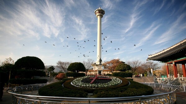 Un grand monument blanc, entouré d’un jardin circulaire orné d’une croix rouge, d’une architecture traditionnelle, et sous un ciel dégagé où volent des oiseaux.