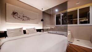 Habitación de hotel moderna con una cama grande, cabina de ducha con paredes de vidrio y un cuadro abstracto de gran tamaño en la pared.