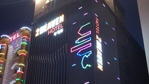 Un hotel con un letrero llamativo que dice "2MEAVEN HOTEL" y una flecha de neón que indica la entrada.