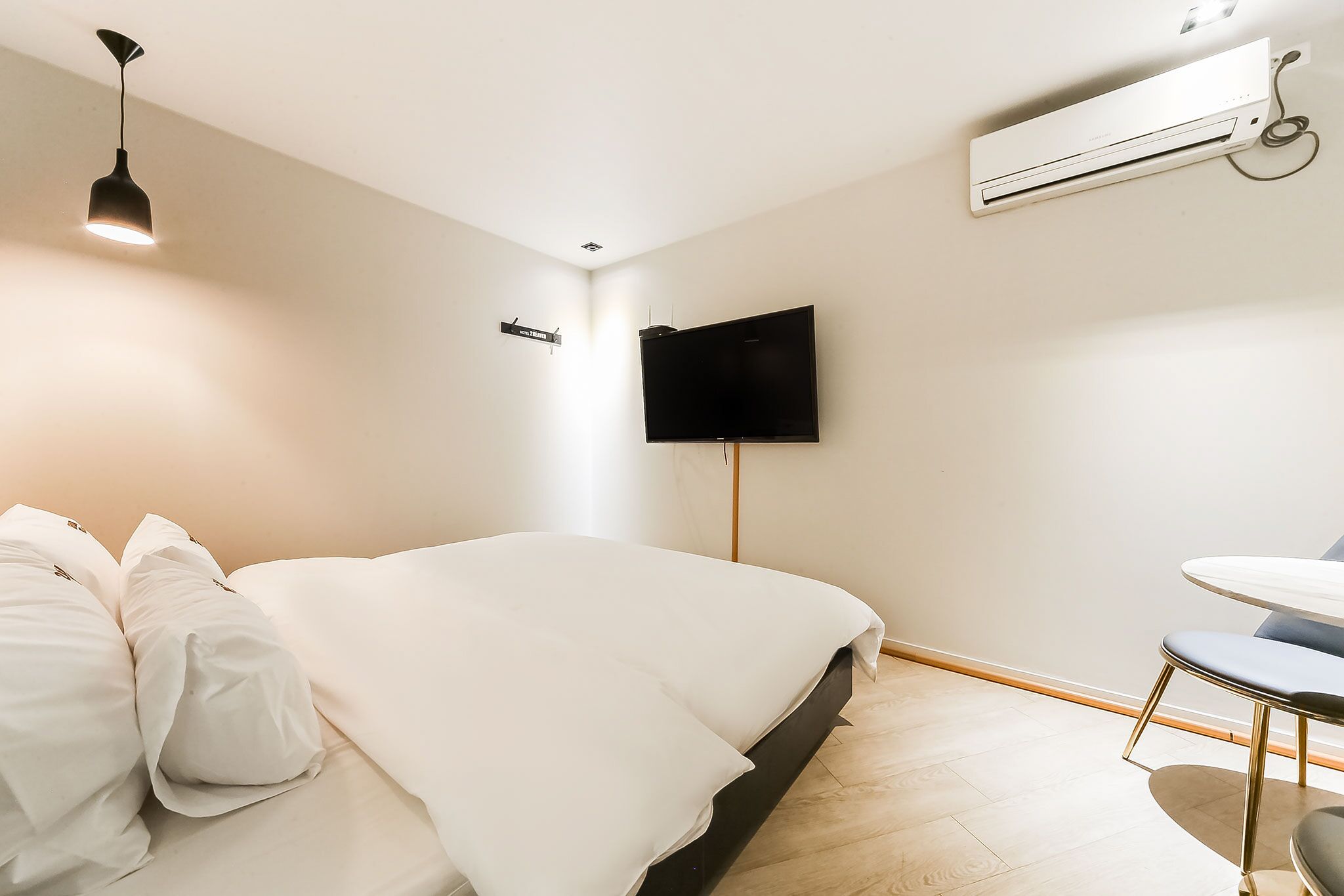Moderni hotellihuone, jossa on sänky, työpöytä, tuoli, taulutelevisio, ilmastointilaite ja riippuvalaisin.