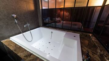 A modern bathroom with a large bathtub, a shower, and a glass partition.