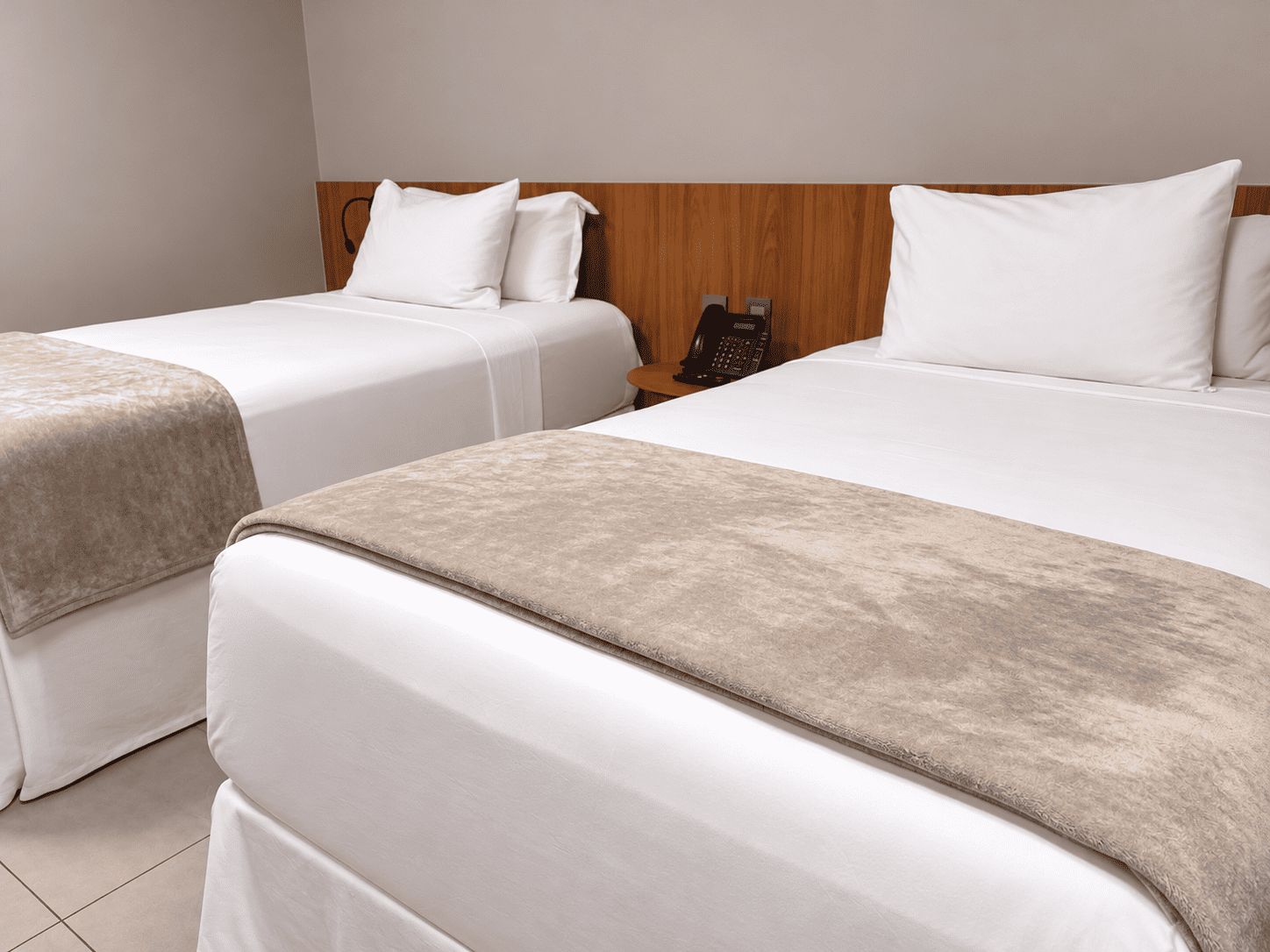 A hotel room with two beds, a wooden headboard, and a telephone on a nightstand.