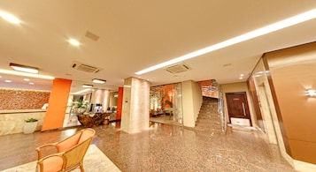 Un vestíbulo de hotel con una recepción, zona de estar y una escalera que conduce a los pisos superiores.