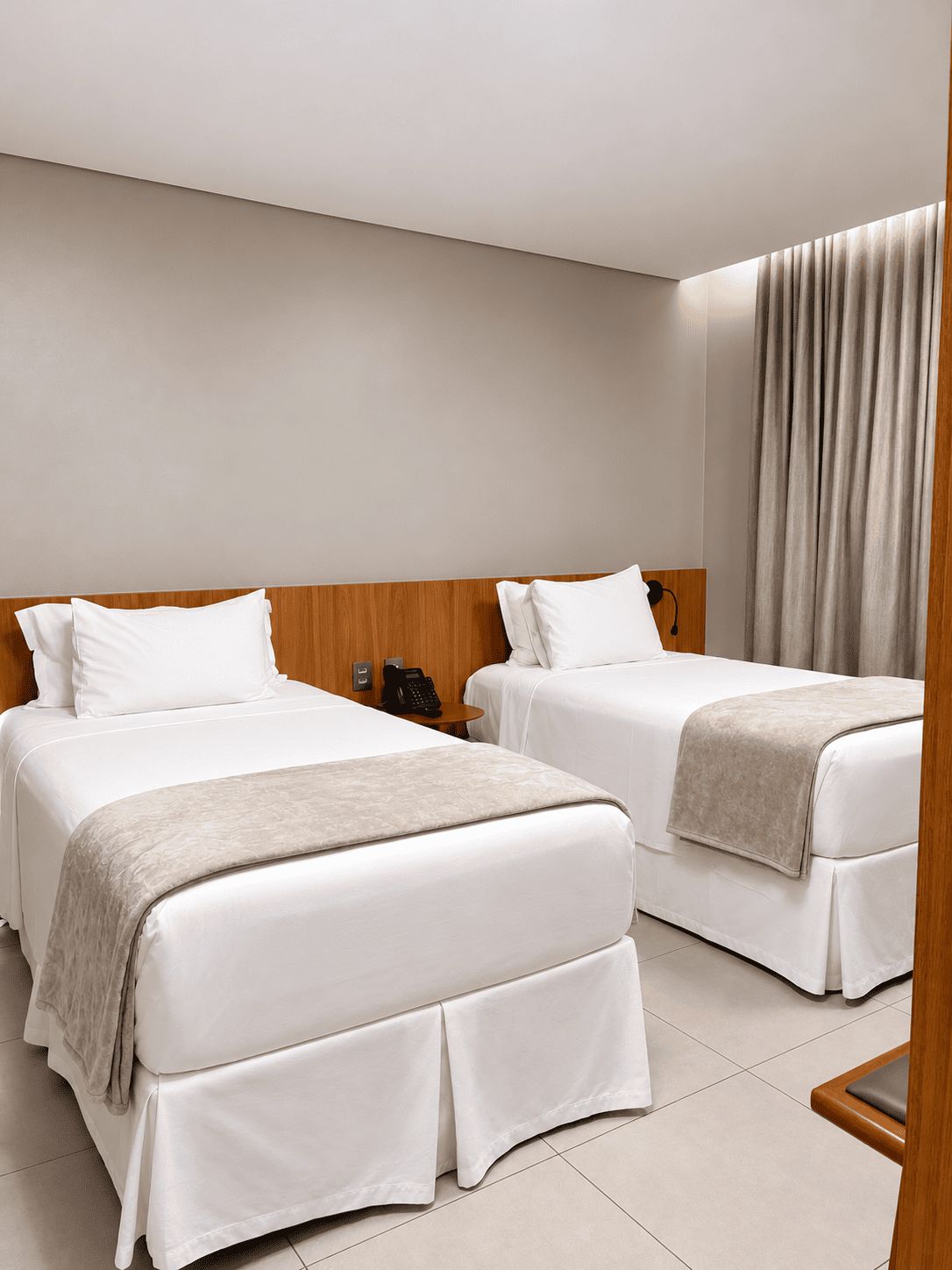 A hotel room with two beds, a wooden headboard, a telephone, and a curtain.