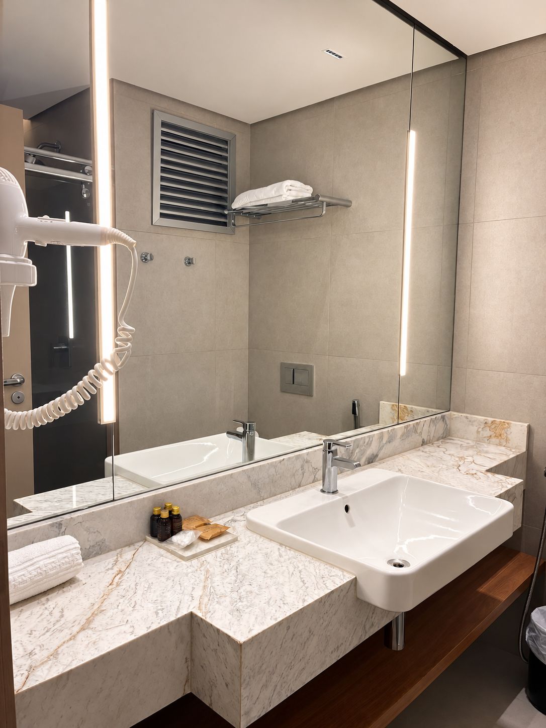 A modern bathroom with a large mirror, two sinks, and a hairdryer.