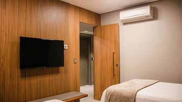 Hotellihuone, jossa on puupanelilla verhoiltu seinä, seinälle asennettu litteänäyttöinen televisio ja sängyssä beige värinen peitto.