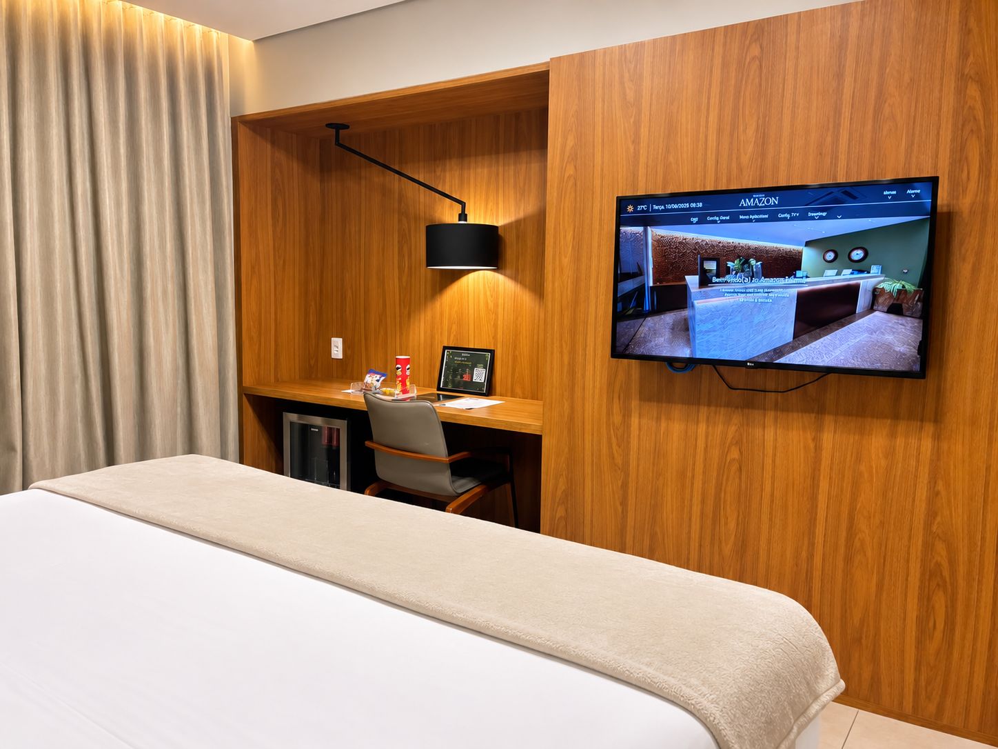 A hotel room with a bed, a desk with a computer, a TV mounted on the wall, and a wooden panel design.