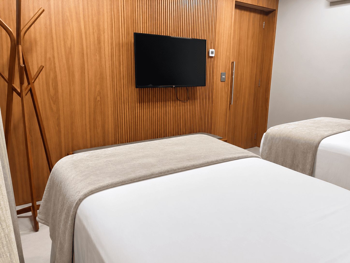A hotel room with two beds, a wooden wardrobe, and a flat-screen TV mounted on the wall.