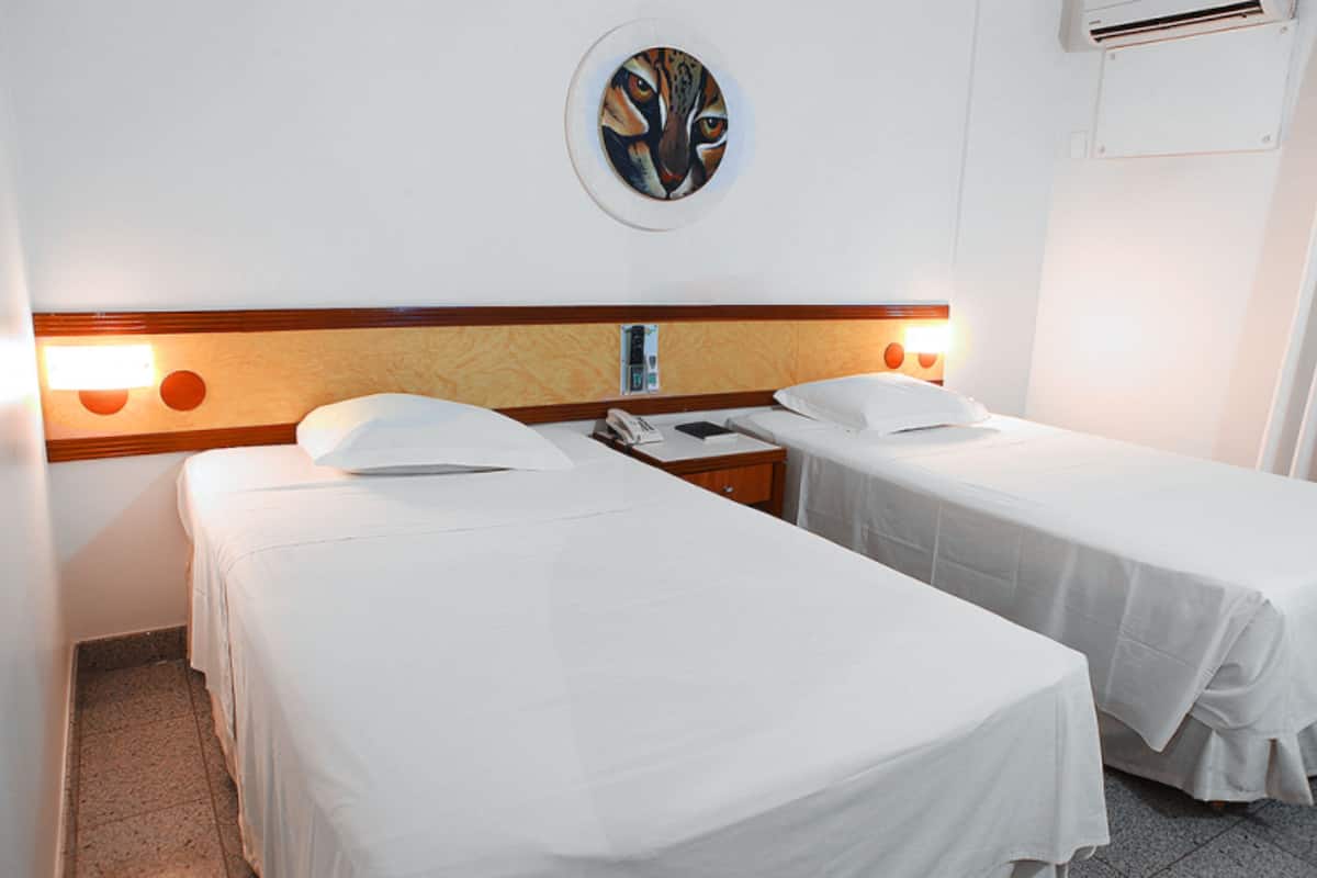 Une chambre d’hôtel avec deux lits simples, une tête de lit en bois, une œuvre d’art accrochée au mur et une table de chevet avec un téléphone.