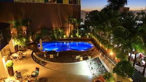 A pool area with lounge chairs and tables, surrounded by palm trees and a stone wall. - Hotel Taiamã (Cuiabá)