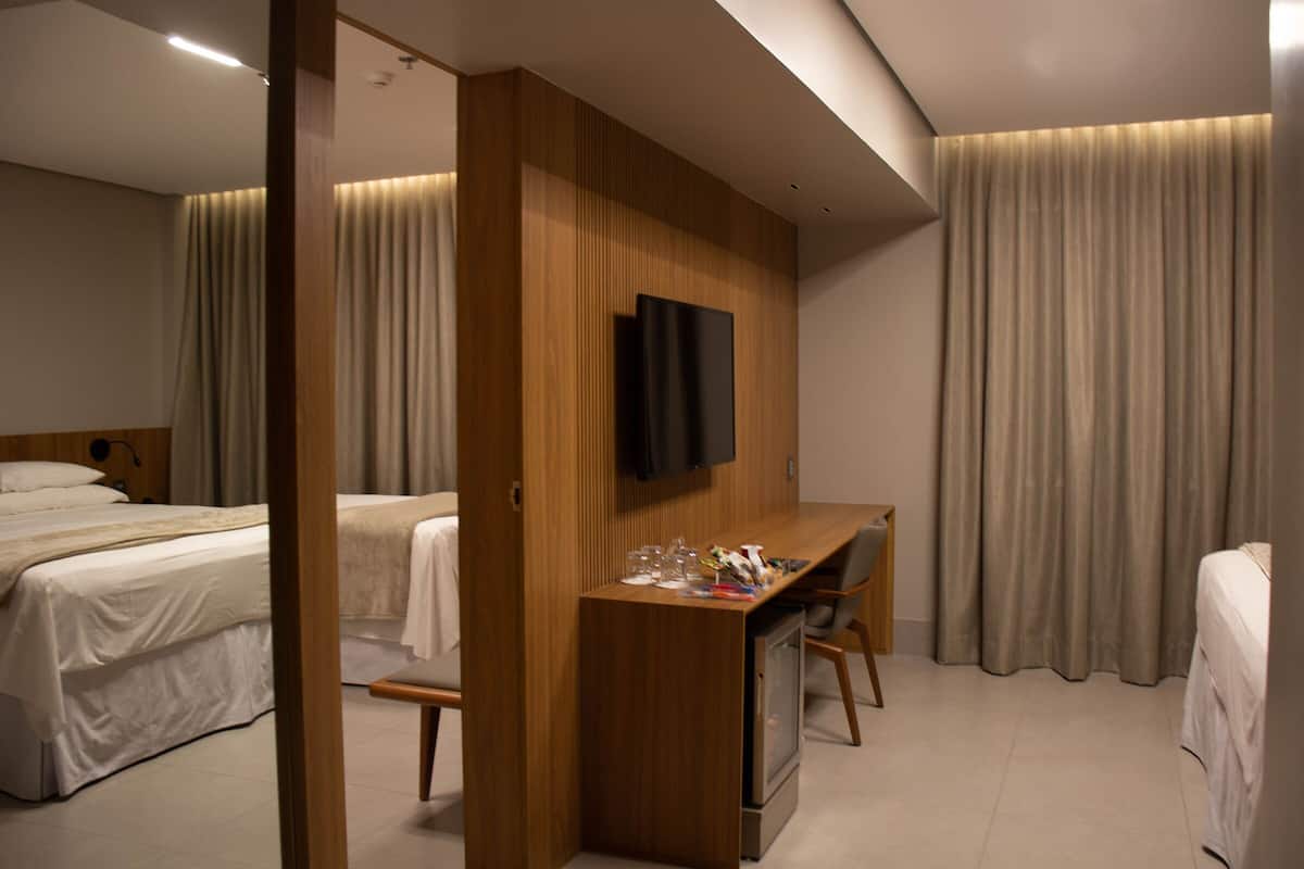 Une chambre d’hôtel avec un lit, un bureau avec une télévision et une fenêtre avec des rideaux.