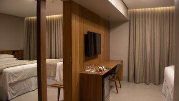 A hotel room with a bed, a desk with a TV, and a window with curtains.