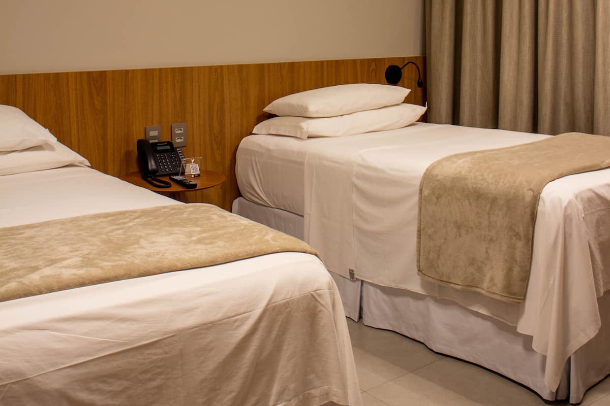Une chambre d’hôtel avec deux lits, un téléphone sur la table de chevet et un rideau.