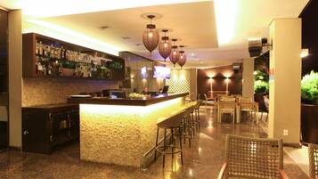 A bar area with a counter, stools, and a television screen.
