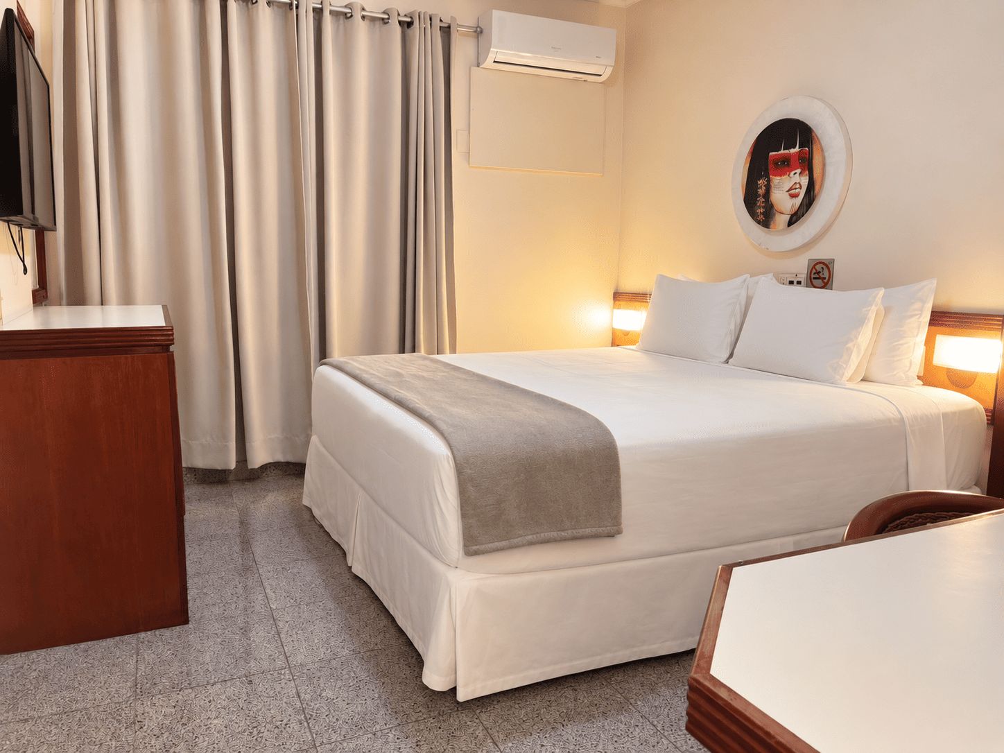 Una habitación de hotel con cama, escritorio, televisor y aire acondicionado.