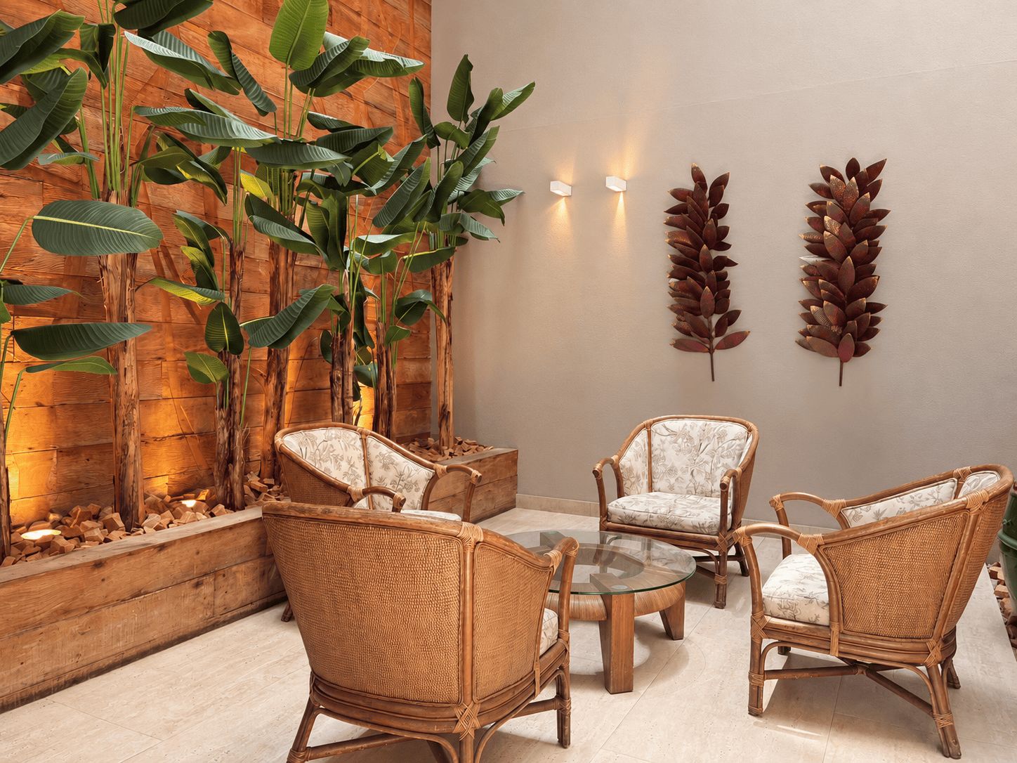 Une pièce meublée de meubles en osier, avec une table en verre et de grandes plantes à feuilles larges.