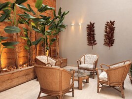 Quarto com móveis de vime, mesa de vidro e plantas grandes e folhosas.