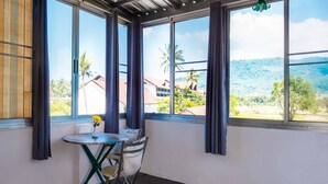 A room with large windows, a small table with a chair, and a view of a mountainous landscape. - Sabina Guesthouse (Kamala)