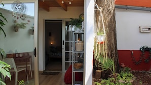 Une porte vitrée donne accès à une pièce dont le sol est en bois, où l’on trouve un banc rouge et une étagère avec des paniers et une plante.