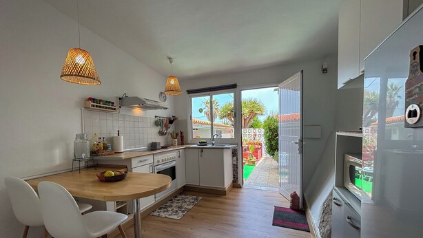 Une cuisine moderne avec des meubles blancs, une table à manger en bois et deux lampes suspendues.