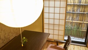 Ein traditioneller japanischer Raum mit Tatami-Bodenbelag, einem niedrigen Tisch, einem Stuhl, einem Shoji-Bildschirm und Blick auf Bambus.