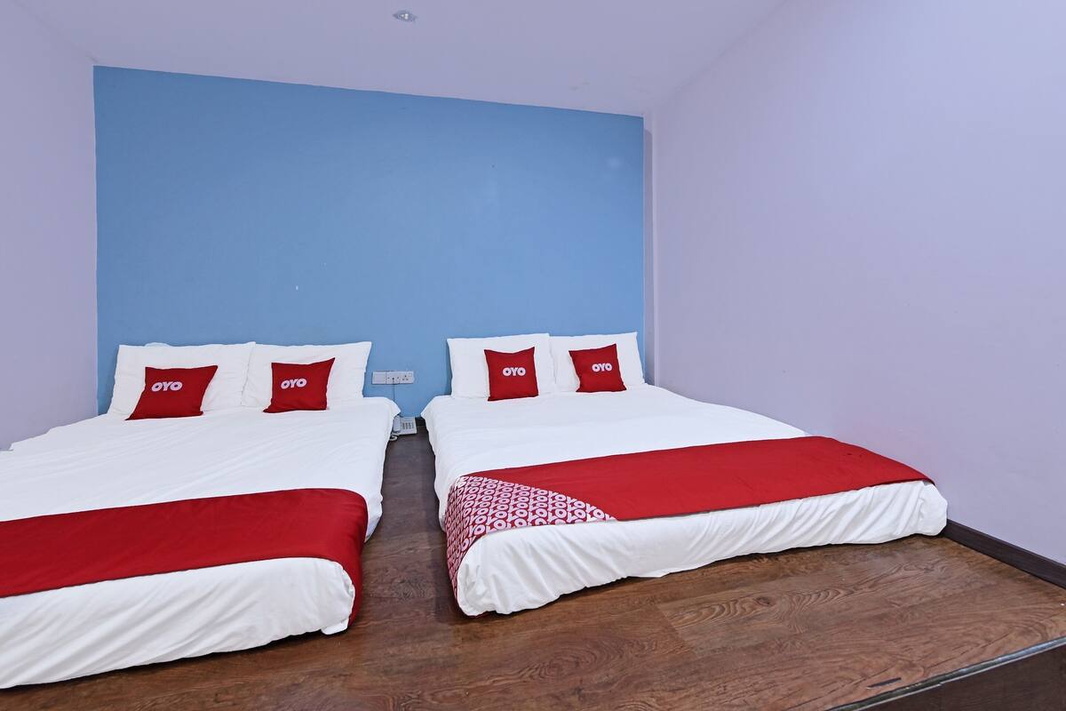 A hotel room with two beds, each with white bedding and red accents, and a blue accent wall.